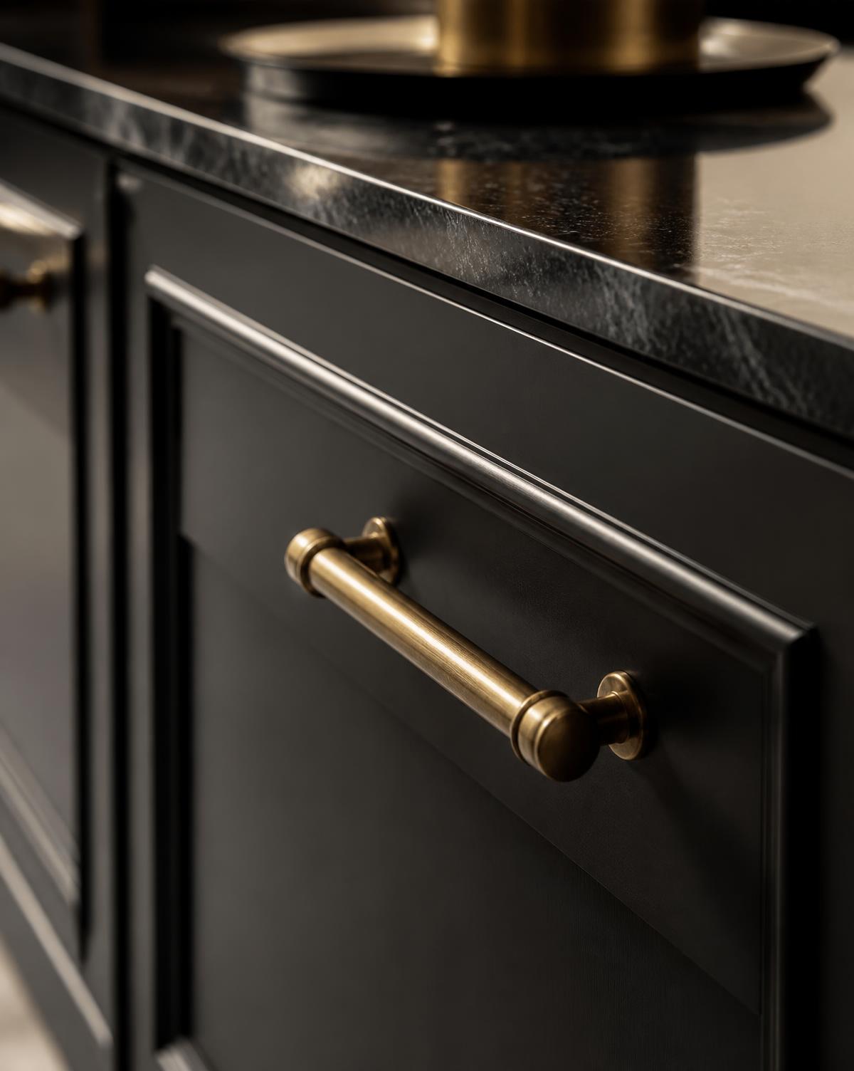 Antique brass handle on a matte black in-frame cabinet door beside a dark stone worktop
